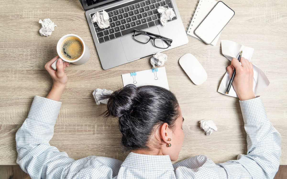 Woman lying on a table in front of a laptop and scrunched up paper
