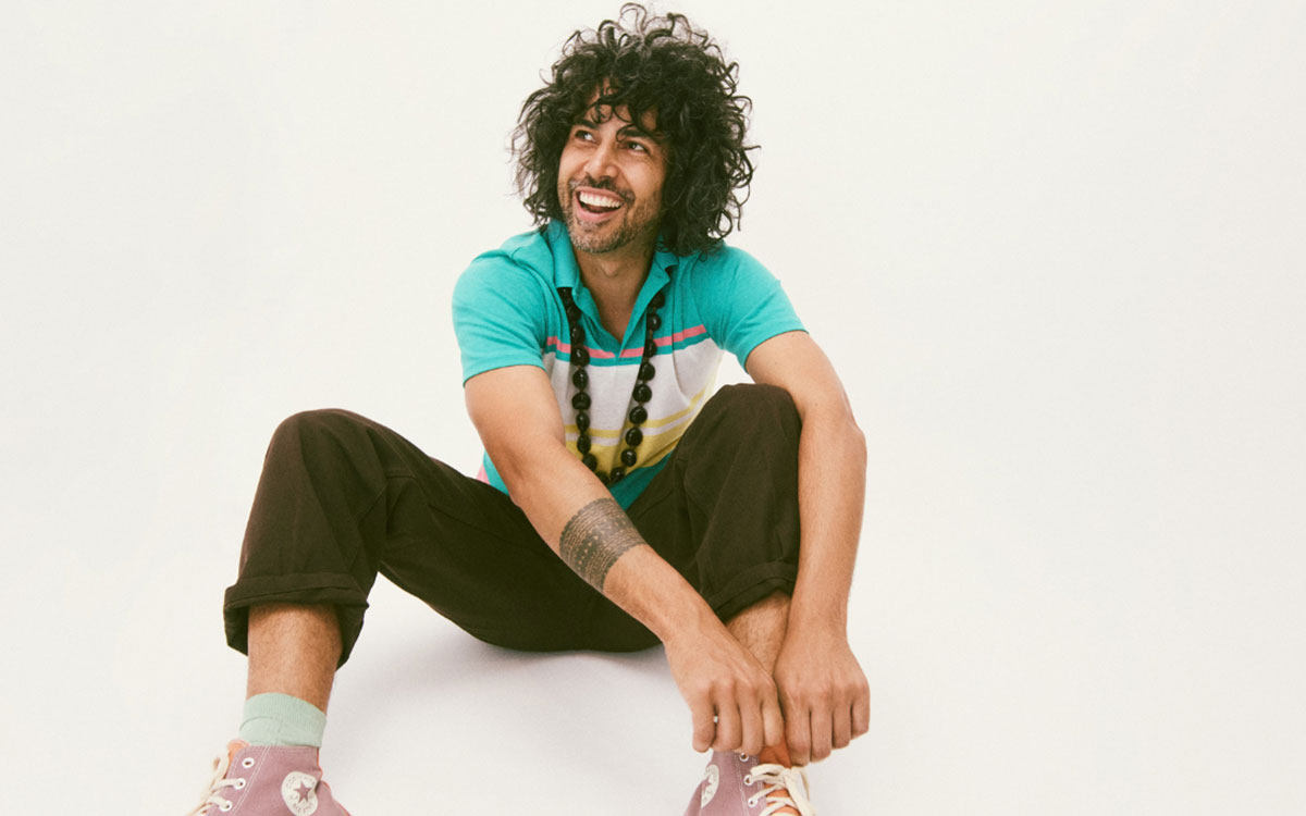 Male performer sitting on the floor with a green shirt and pink shoes