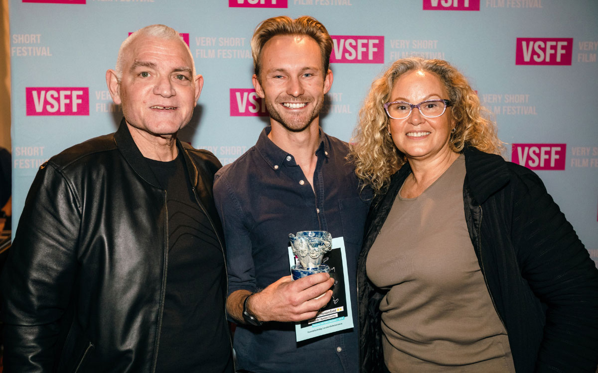 Two men and a woman standing in front of VSFF signage smiling