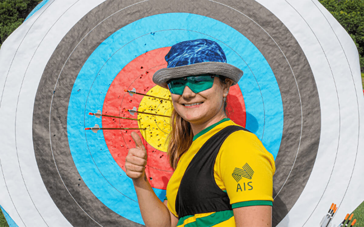 Imogen Grzemski standing in front of an archery board giving a thumbs up