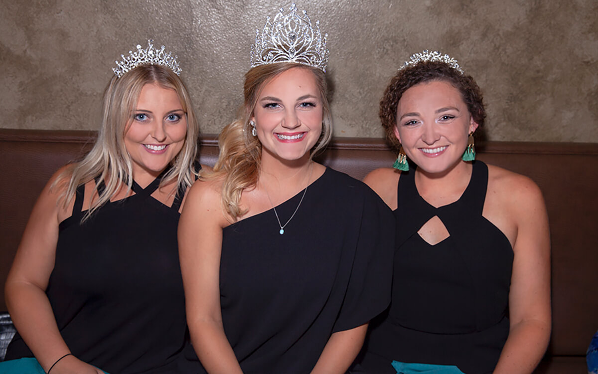 Three girls wearing black dresses and tiaras