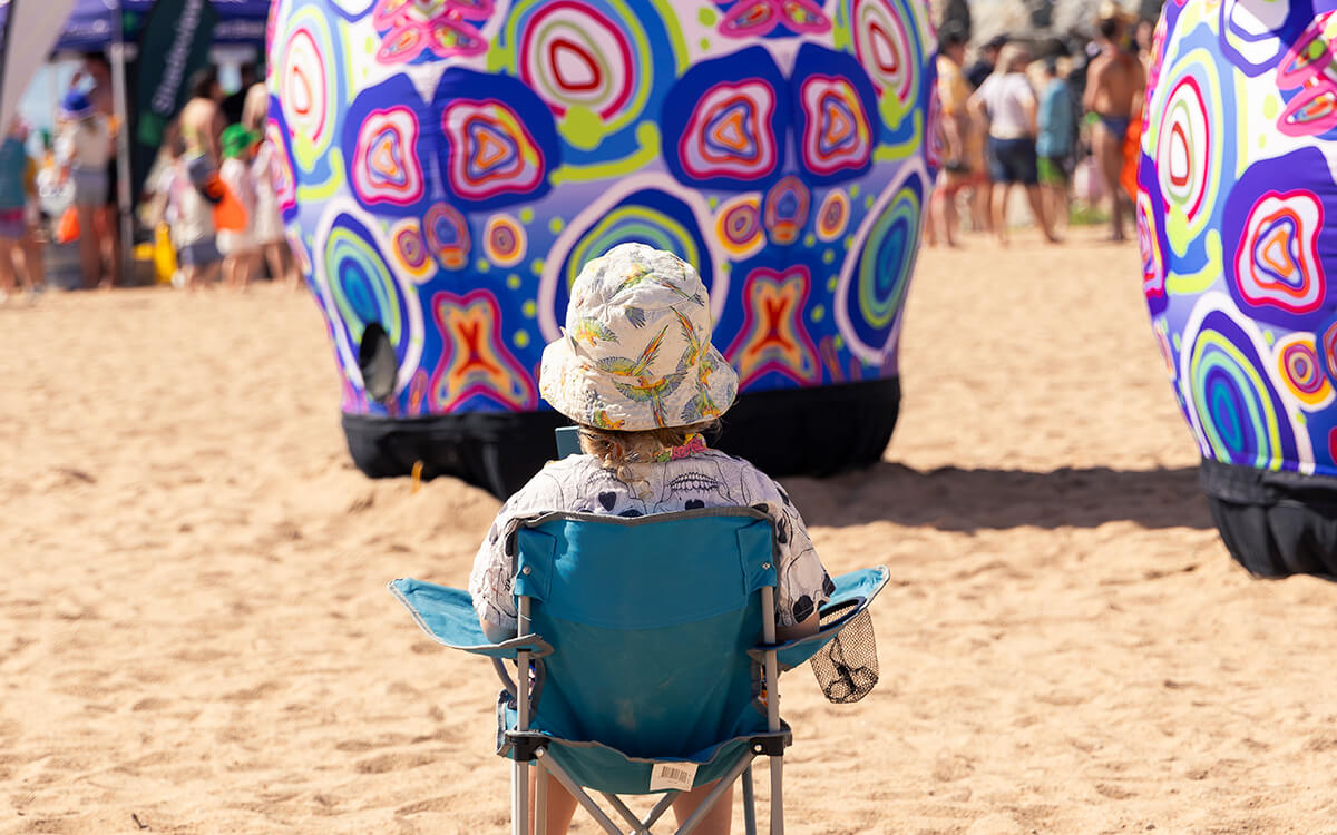 Small child with their back to the camera sitting in a chair on The Strand looking at Ephemera art