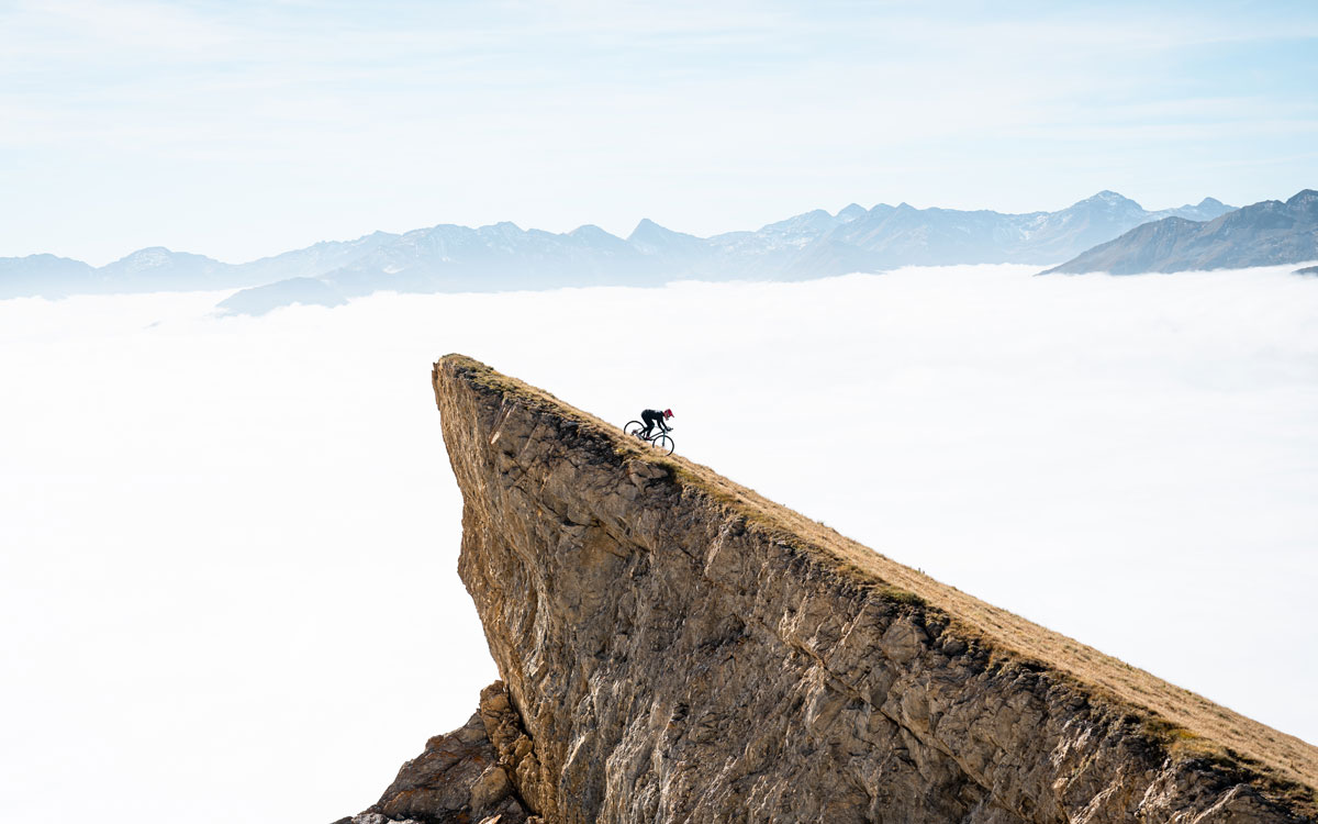 A cyclist on a very steep slope against a misty backdrop of mountains